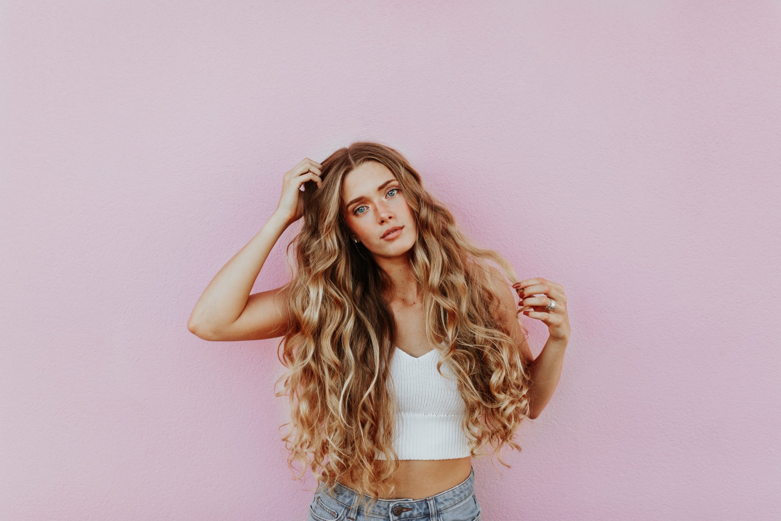 Mujer de cabello largo y rizado sobre fondo rosa