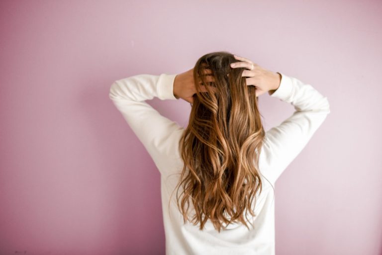 Mujer con el cabello largo de espaldas sobre fondo rosa