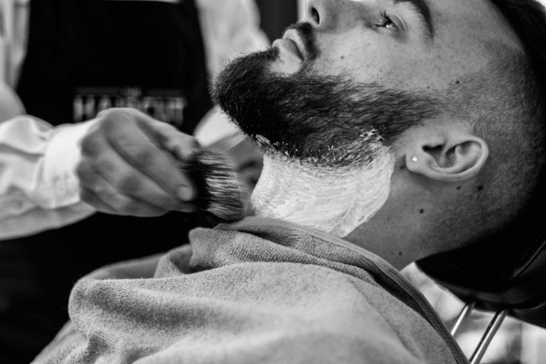Barbero poniendo espuma de afeitar sobre el rostro de un cliente